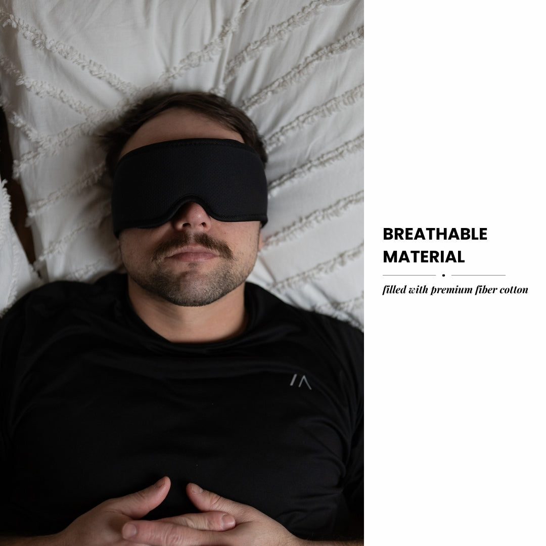 Man wearing a black sleep mask lying on a bed with text about breathable material.
